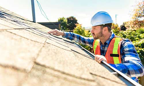 Worker with an orange vest and hard hat inspecting a residential roof